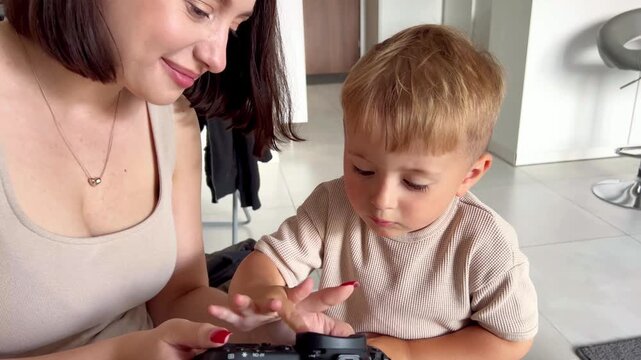  A loving mother and her child enjoy a joyful moment together, smiling and laughing while looking at photos on a digital camera. Captured in natural light at home, this cand