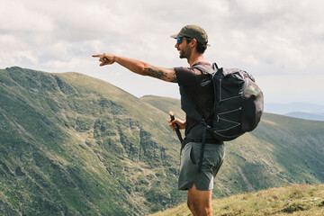 A hiker with backpack points towards a majestic mountain range on a cloudy day.  Epic adventure and exploration concept. Ideal for travel, outdoor, and lifestyle projects.