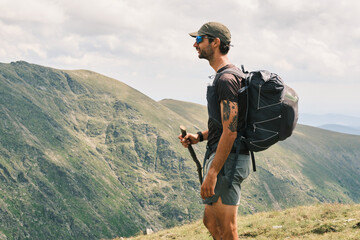 A lone hiker pauses on a mountain trail, taking in the breathtaking panoramic view.  His backpack...
