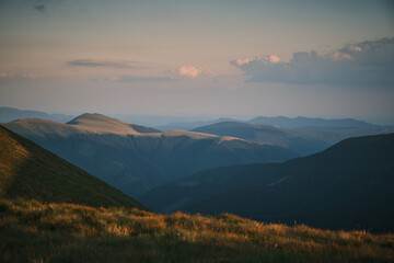 Fototapeta premium Serene sunset over rolling mountain ranges. Golden hour light bathes the landscape in a warm glow. Perfect for travel, nature, or inspirational projects.