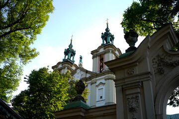 Baroque towers rise in prayer. Light grazes ornate façades. Trees frame silent reverence. The...