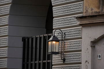 Vintage wall lantern glows softly against textured facade. Classic wrought iron frame adds charm to...