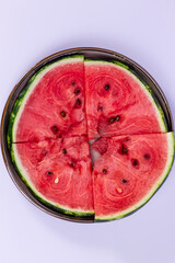 Four juicy slices of vibrant red watermelon with black seeds are arranged in a circular pattern on a round metal tray. Refreshing summer fruit.