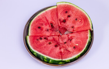 Four slices of red watermelon, some with black seeds, are arranged on a round, dark-rimmed tray,...