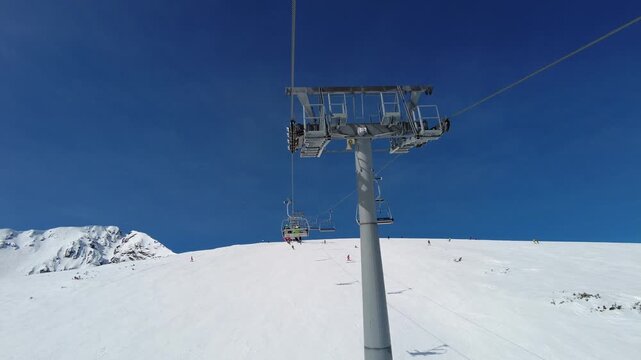 4K video clip of four person ski chair lift going over mountain pistes in a ski resort with a blue sky