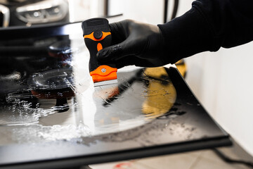 Technician uses scraper to clean the surface of a new windshield post-replacement. Technician...