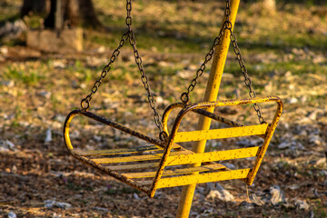 Rusty iron chair hanging from a swing for a playground kids in a public square in Brazil
