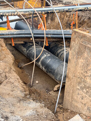Construction site showing large black pipes laid in a trench, surrounded by dirt and wooden...