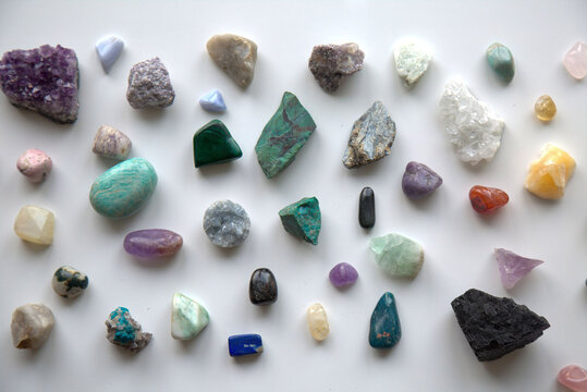 A neatly arranged assortment of polished and raw crystals displayed on a white background. Featuring a variety of colors and textures, this image is ideal for themes related to wellness, energy healin