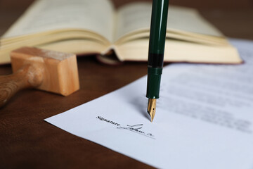 Signing notary document with fountain pen at leather surface against brown background, closeup