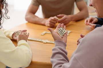 Friends playing dominoes at wooden table indoors, closeup