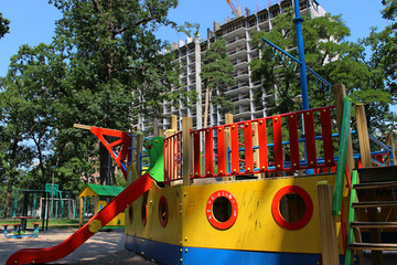  Sand covered multi colored playground with slides and small merry go round in front of frame of...