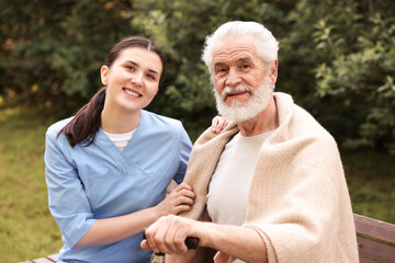 Obraz premium Smiling nurse with elderly man on bench outdoors