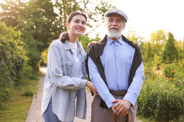 Portrait of smiling caregiver and elderly man with walking cane outdoors