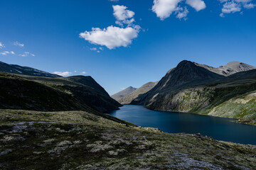 Summer in Norway, rugged rocky mountains surrounding a highland lake dyed dark blue, colorful tents on the lakeside, Rondvatnet, Rondane, Norway