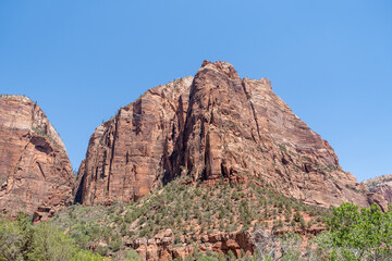 The steep, jagged peak of a Zion mountain juts into the sky, highlighted in warm tones under the...