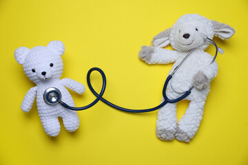 Pediatrics concept. Toy sheep and bear with stethoscope on yellow background, top view