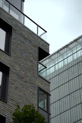Architectural detail of modern building with stone and glass facade. Metal-framed windows reflect light, complemented by a nearby green tree and minimalist balcony design.

