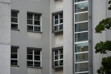 Close-up of light gray building facade with several double-pane windows featuring white frames. The...
