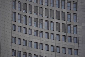 Close-up of modern office building windows with gray stone facade. Vertical window blinds partially cover some windows, emphasizing symmetry and sleek architectural detail.

