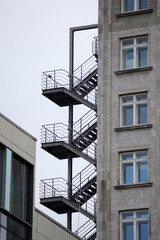 Outdoor metal fire escape staircase attached to urban buildings with multiple landings and...