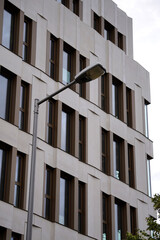Modern street lamp mounted on a tall metal pole beside a contemporary office building with large...