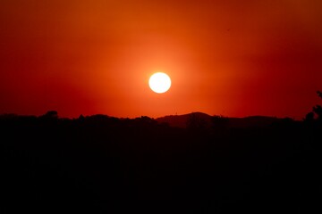 Pôr do sol intenso com céu em tons de vermelho e laranja sobre silhuetas de montanhas. Uma cena dramática e serena, perfeita para representar a beleza natural, a paz e a contemplação.