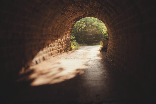 Sunlight illuminates the path at the end of a dark stone tunnel, symbolizing hope and new beginnings
