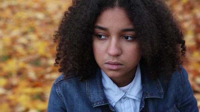 Beautiful mixed race African American girl teenager young woman wearing a blue denim jacket outside sad or depressed