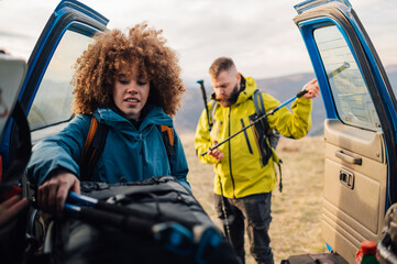 Hikers preparing for trekking, unpacking gear from car trunk