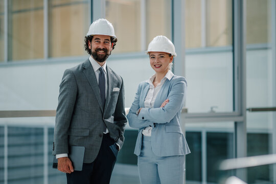 Smiling engineers wearing hard hats and formal wear in modern office building