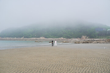 In June 2025, a Korean man and woman in their late fifties walk along the peaceful seashore,...