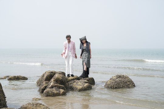 In June 2025, a Korean man and woman in their late fifties are playing together along the rocky shoreline, stepping over jagged stones and enjoying the coastal scenery in Incheon Metropolitan City.