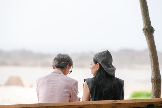 In June 2025, a Korean man and woman in their late fifties sit on a bench by the sea, chatting and smiling as they enjoy the breeze, ocean view, and calm surroundings in Incheon Metropolitan City.
