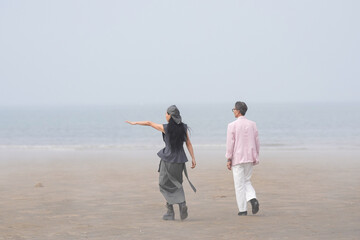 In June 2025, a Korean man and woman in their late fifties walk along the peaceful seashore, enjoying the soft ocean breeze, quiet moments, and each other's company in Incheon Metropolitan City.