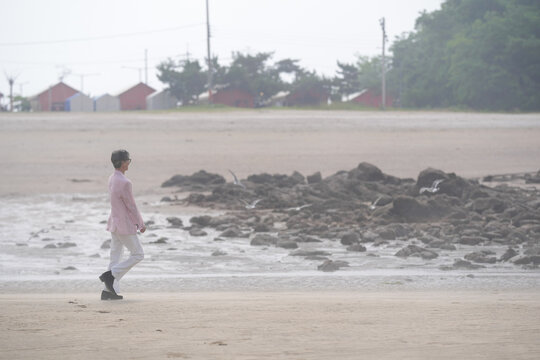 In June 2025, a Korean man and woman in their late fifties walk along the peaceful seashore, enjoying the soft ocean breeze, quiet moments, and each other's company in Incheon Metropolitan City.