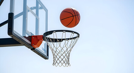 Fototapeta premium A basketball is flying through the air towards a basketball hoop against a clear blue sky background