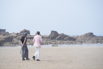 In June 2025, a Korean man and woman in their late fifties walk along the peaceful seashore, enjoying the soft ocean breeze, quiet moments, and each other's company in Incheon Metropolitan City.