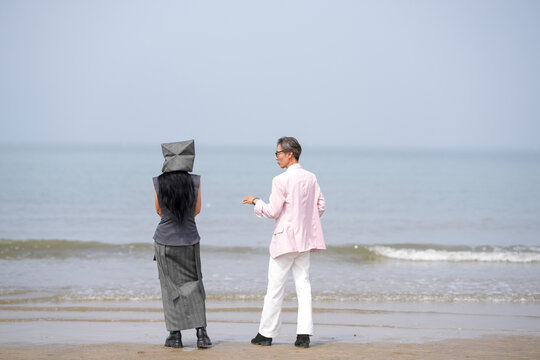 In June 2025, a Korean man and woman in their late fifties are standing and talking beside the rugged shoreline filled with jagged rocks and crashing waves in Incheon Metropolitan City, South Korea.