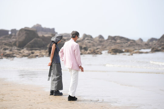 In June 2025, a Korean man and woman in their late fifties are standing and talking beside the rugged shoreline filled with jagged rocks and crashing waves in Incheon Metropolitan City, South Korea. - Powered by Adobe