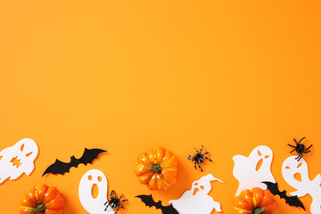 Halloween flat lay on vibrant orange background: pumpkins, black bats, white ghosts, and spiders evoke spooky charm