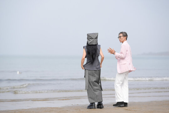 In June 2025, a Korean man and woman in their late fifties are standing and talking beside the rugged shoreline filled with jagged rocks and crashing waves in Incheon Metropolitan City, South Korea.
