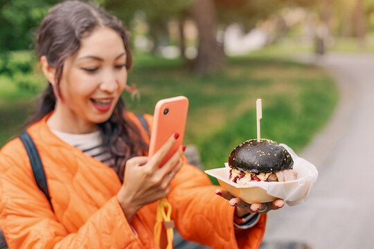 Happy tourist capturing a photo of a delicious black burger with her smartphone