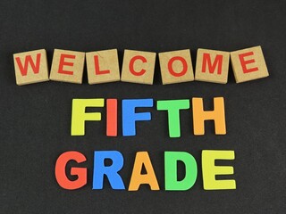 Wood letters form the word "Welcome" and multicolored eva foam letters form the expression "Fifth grade", referring to the elementary school days on black background. Back to school concept.