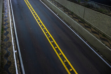 Dark street with yellow lines. Road marking on black asphalt. Urban scene in Brazil