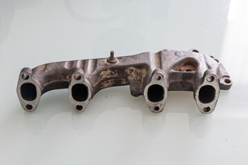 A rusty cast iron exhaust manifold with freshly machined, straightened port faces, lying on a glossy white surface for display or inspection.