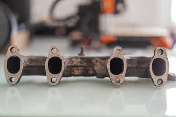 A rusty cast iron exhaust manifold with freshly machined, straightened port faces, lying on a glossy white surface for display or inspection.