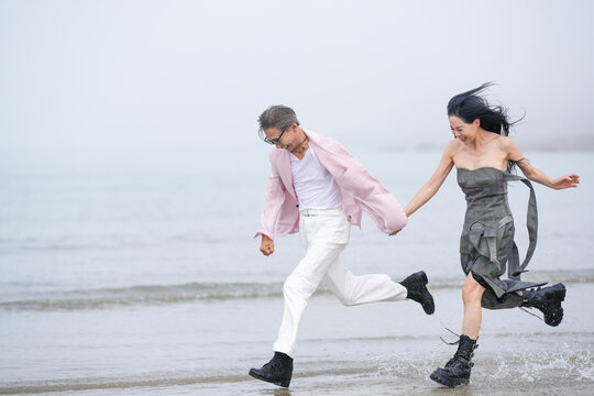 In June 2025, a Korean man and woman in their late fifties are running at full speed along the rugged shoreline filled with jagged rocks and crashing waves in Incheon Metropolitan City, South Korea.