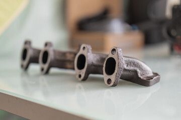A rusty cast iron exhaust manifold with freshly machined, straightened port faces, lying on a glossy white surface for display or inspection.