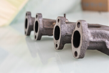 A rusty cast iron exhaust manifold with freshly machined, straightened port faces, lying on a glossy white surface for display or inspection.